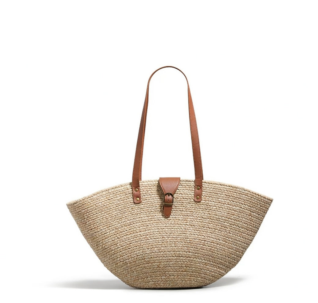 A natural woven straw tote bag with brown leather shoulder straps and a small brown leather front tab, shown on a plain white background.