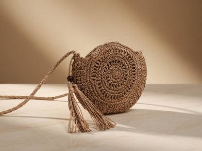 Round woven bag with tassel on a light wooden surface